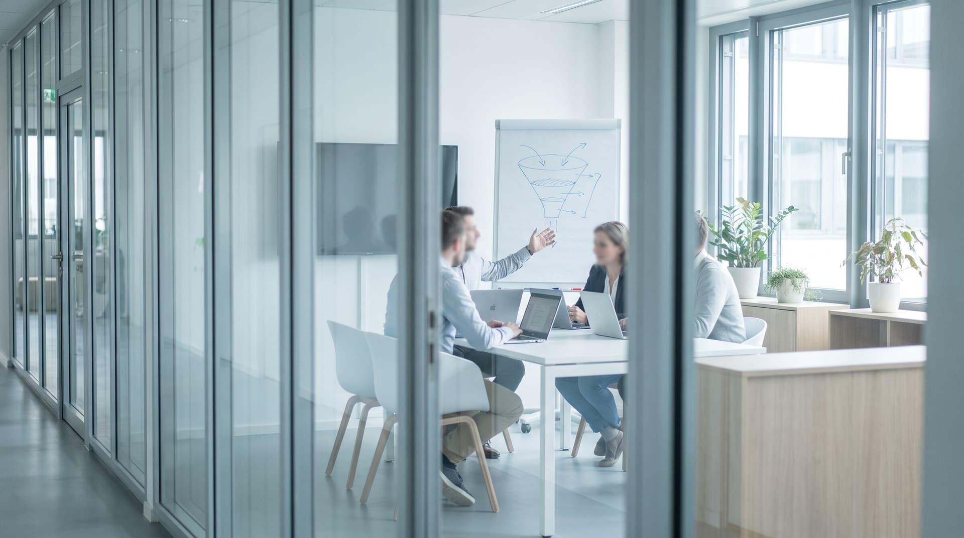 Kleines Team im gläsernen Besprechungsraum vor einem Whiteboard mit Vertriebstrichter